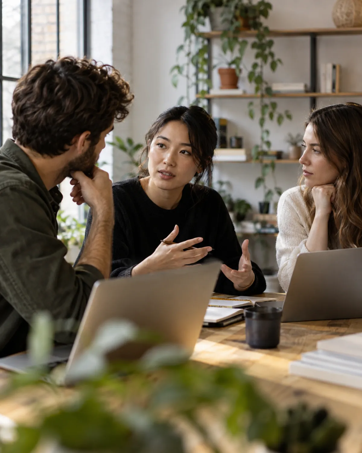 Three colleagues talking at a table with laptops