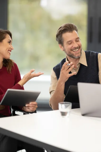 A teacher laughing with a student during a conversation lesson at a bright table